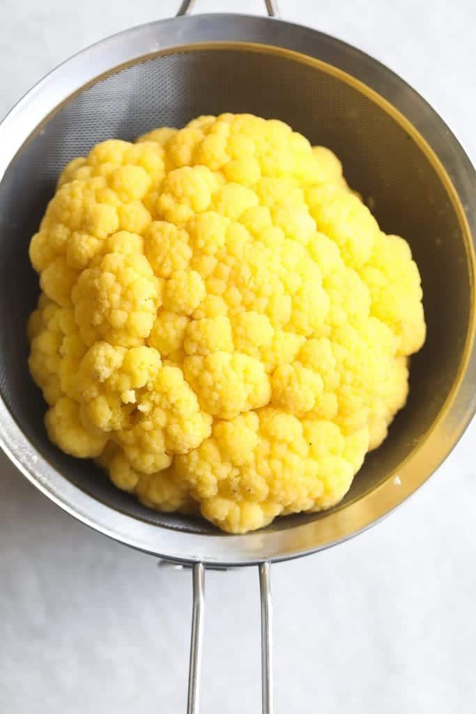 whole cauliflower draining in a colander