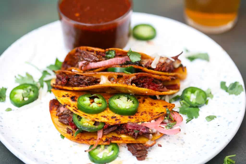 birria tacos on a white plate with jalapenos and cilantro