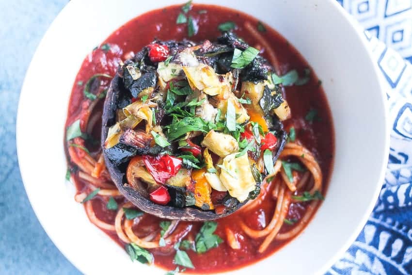 a bowl of spaghetti with pasta sauce topped with a whole portobello mushroom stuffed with vegetables