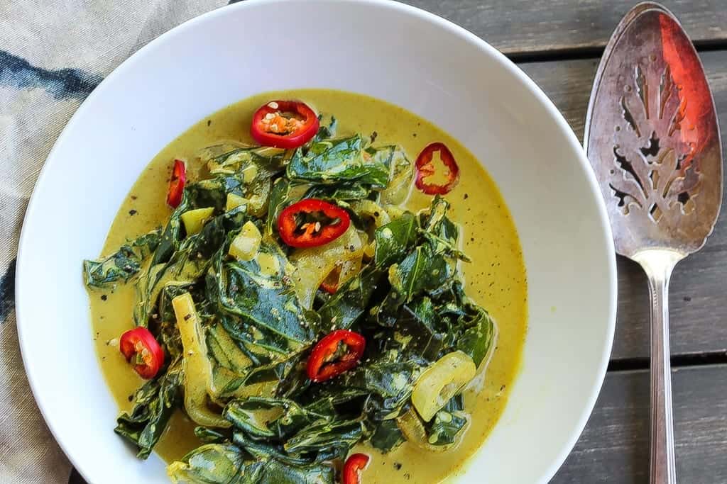 coconut curry braised collard greens in a white bowl topped with red chilis