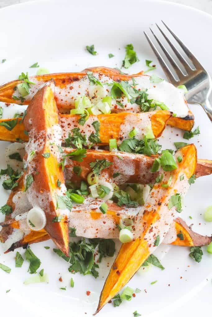 roasted sweet potatoes (wedges) topped with yogurt sauce and green onions on a white plate