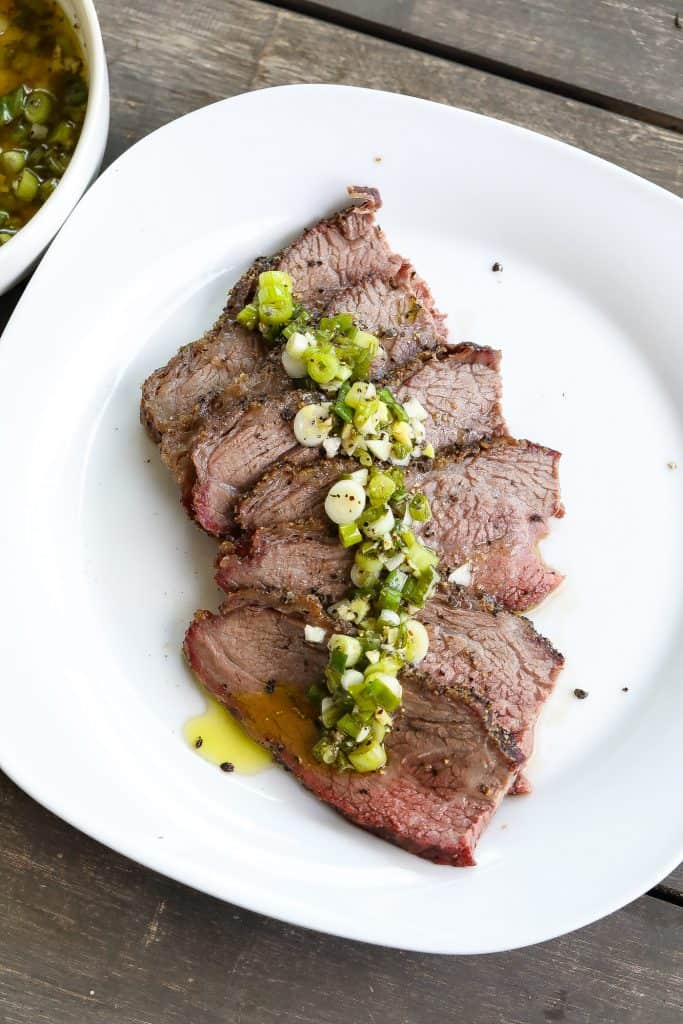 smoked tri tip topped with green sauce on a white plate