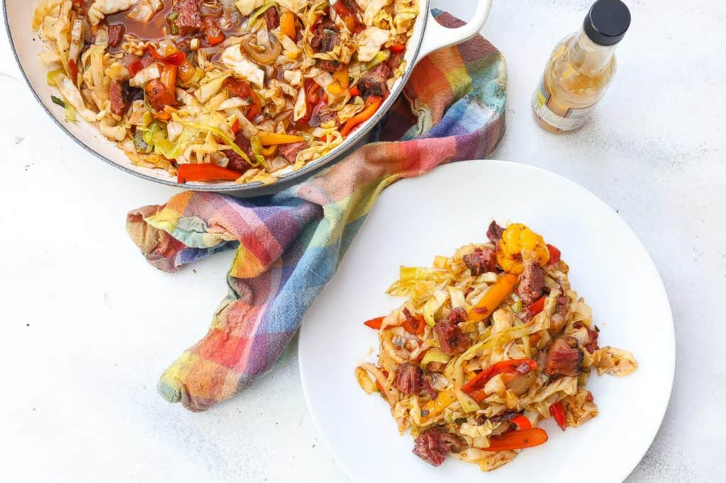 cabbage with corned beef brisket and peppers on a white plate.