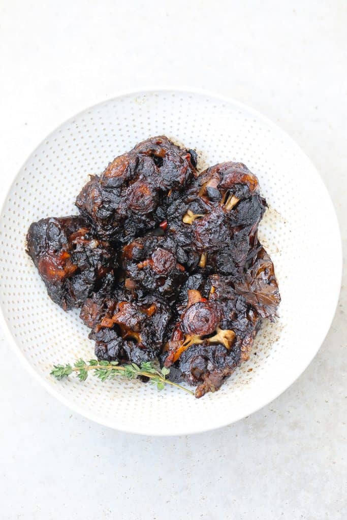 beef oxtail on white plate with fresh thyme