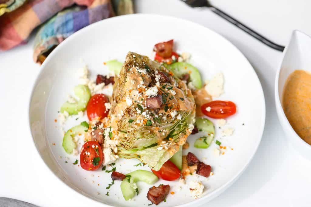 wedge salad on white plate with tomatoes and dressing