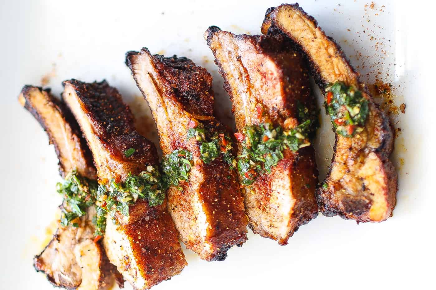 babyback ribs on a white plate topped with chimichurri sauce