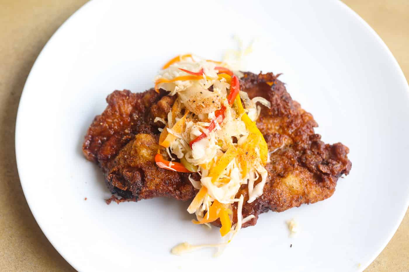 fried pork steak on white plate topped with slaw