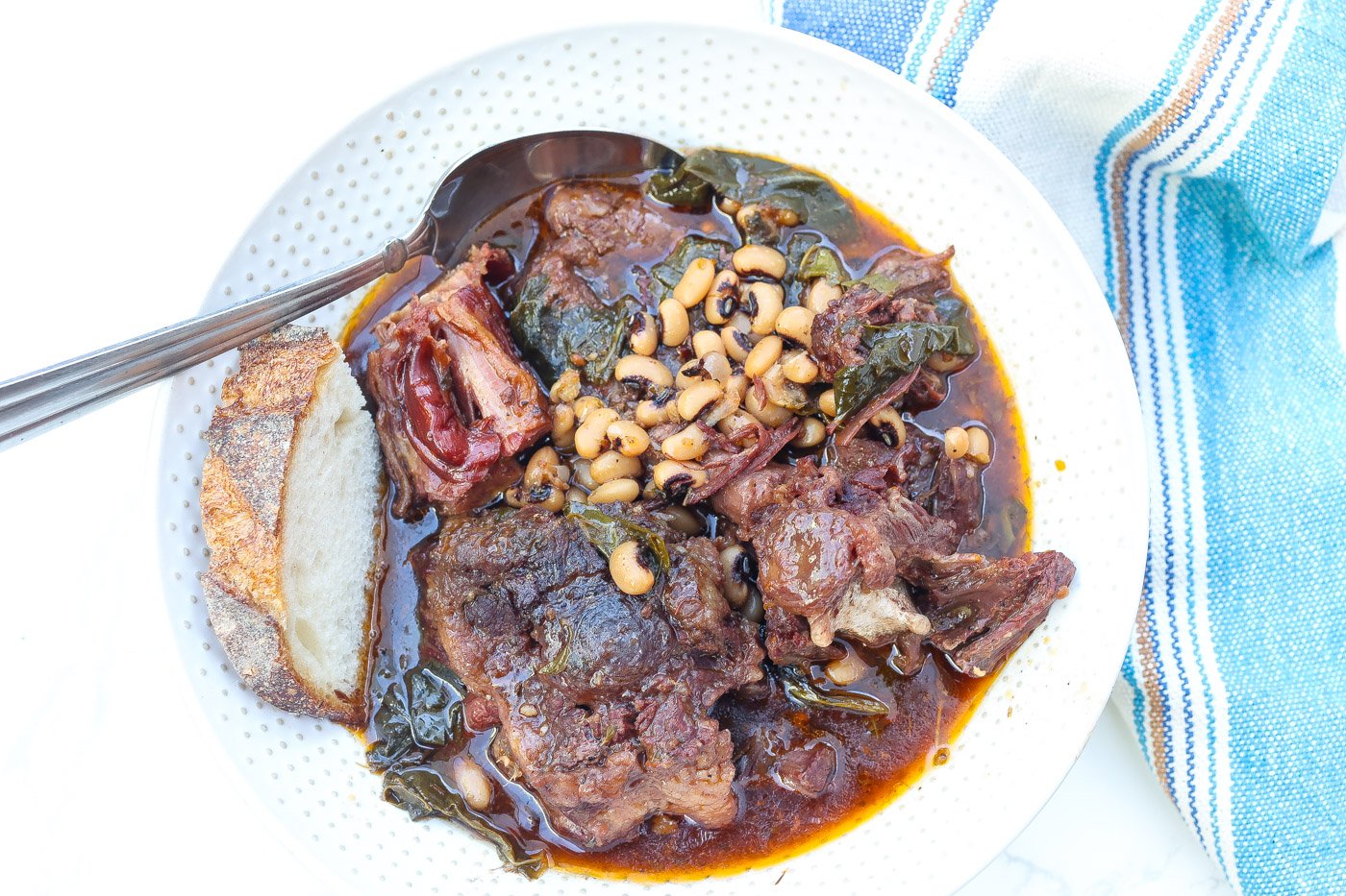 beef oxtail soup with collard greens and blackeyed peas in a white bowl