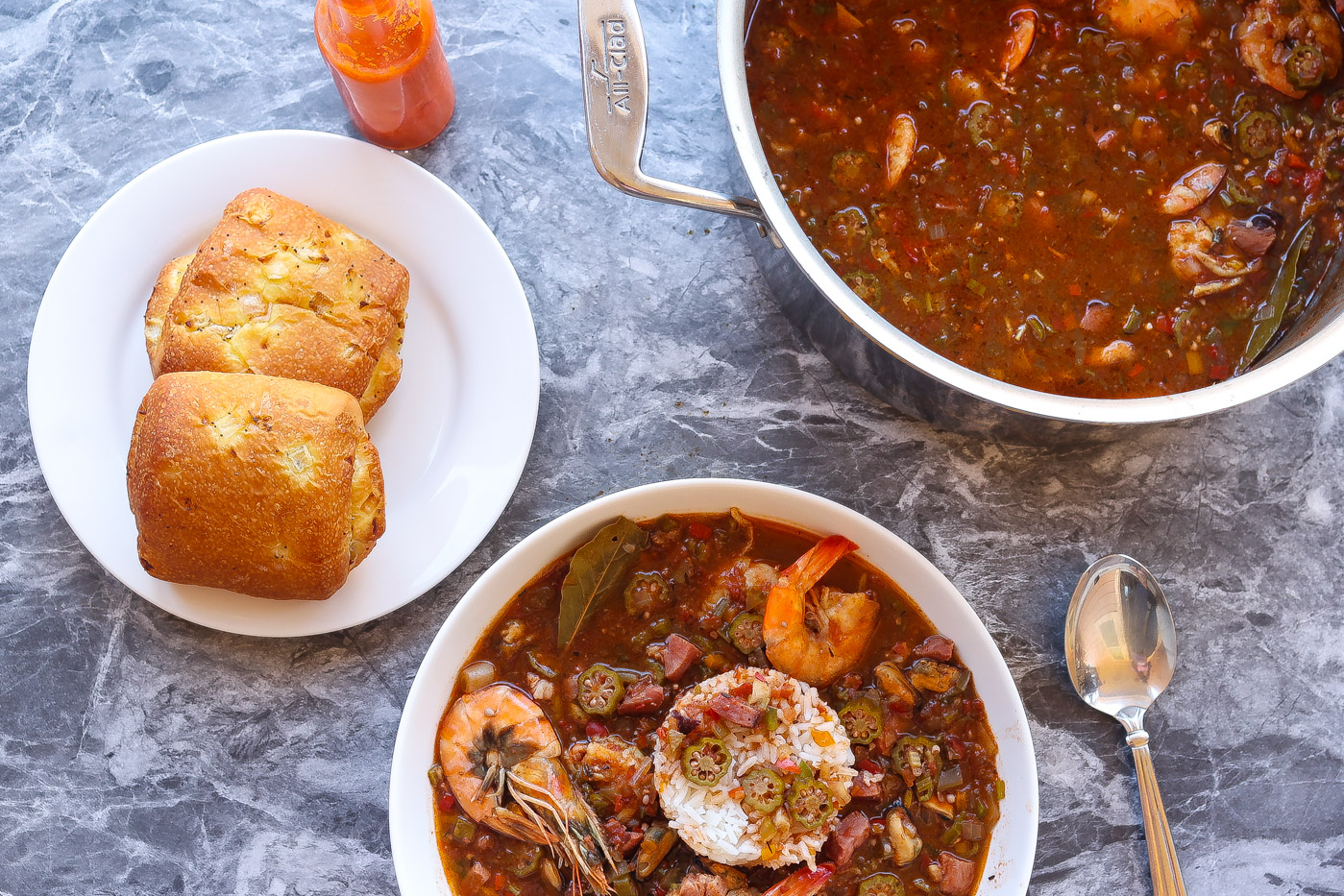 Okra gumbo with shrimp in a white bowl with bread rolls