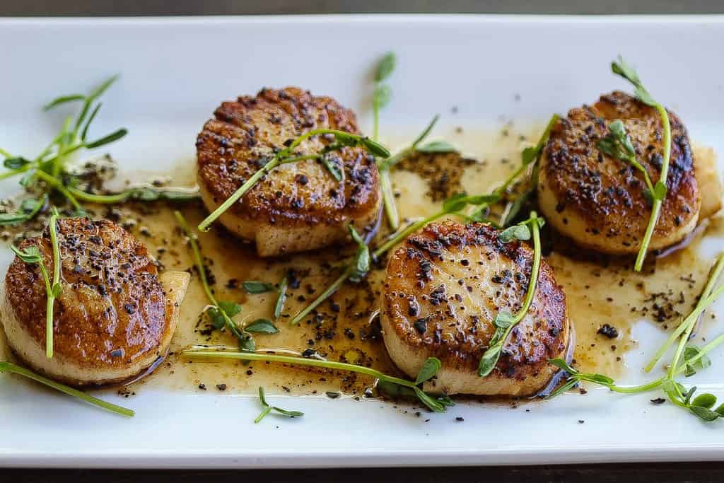 pan-seared scallops on plate topped with herbs and coffee vinaigrette