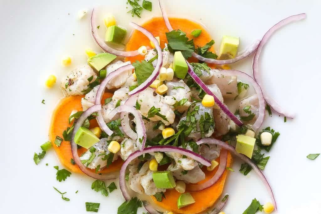 peruvian ceviche on a white plate with sweet potatoes and corn