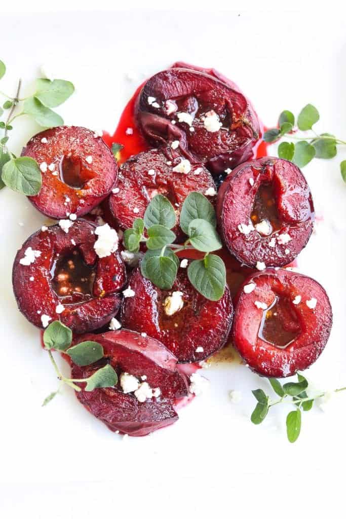 roasted plums topped with feta cheese and syrup on a white plate.