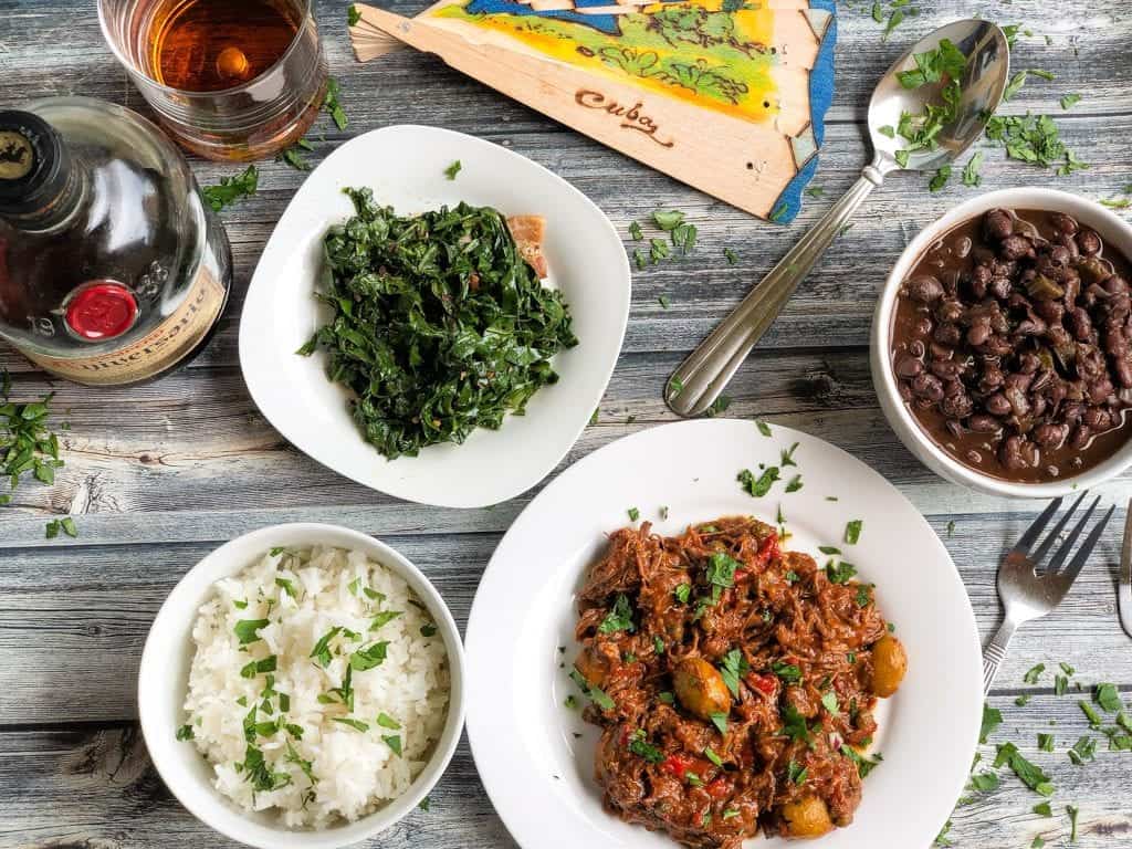 tray with cuban ropa vieja, black beans, rice, greens, and rum