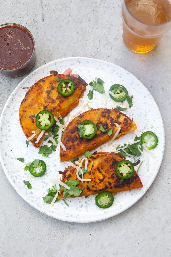 birria tacos on a white plate with jalapenos and cilantro