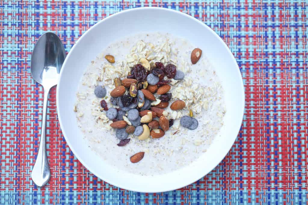 overnight oatmeal with fonio topped with trail mix in a white bowl