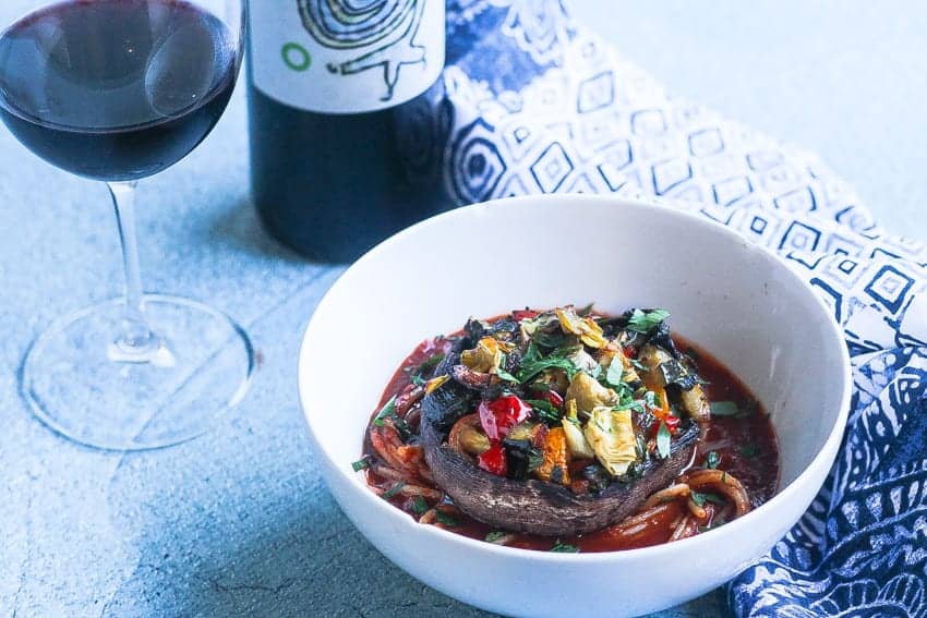 a bowl of spaghetti with pasta sauce topped with a whole vegan stuffed portobello mushroom