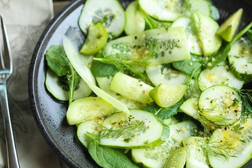 sliced keto cucumber salad in a black bowl with baby spanich and green vinaigrette salad dressing