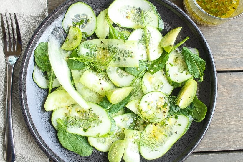 sliced cucumber salad in a black bowl with baby spanich and green vinaigrette salad dressing
