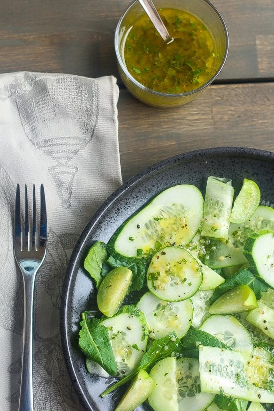 sliced keto cucumber salad in a black bowl with baby spanich and green vinaigrette salad dressing