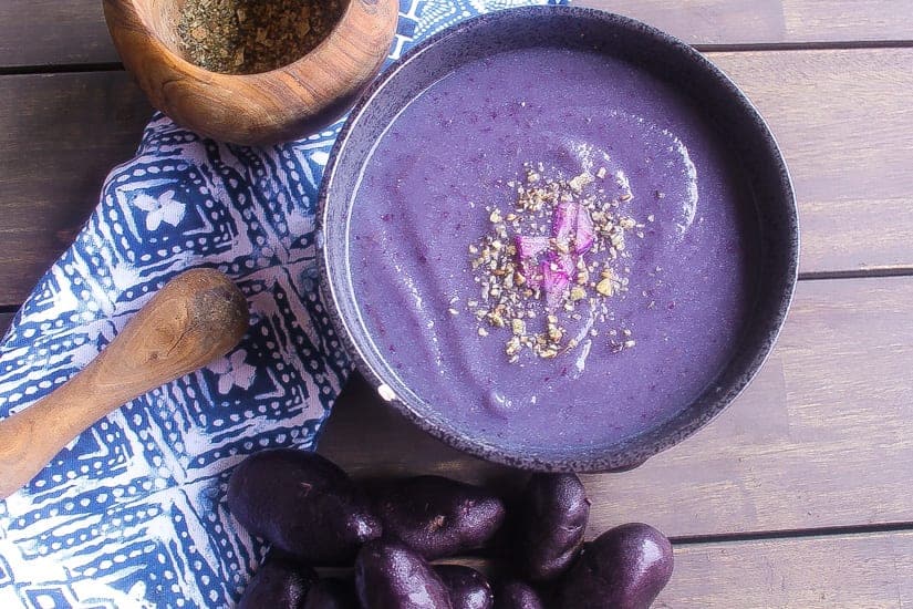 purple soup with purple cauliflower & purple potatoes in black bowl topped with spices 
