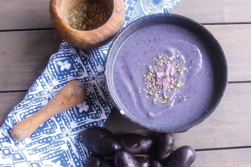 purple soup with purple cauliflower & purple potatoes in black bowl topped with spices
