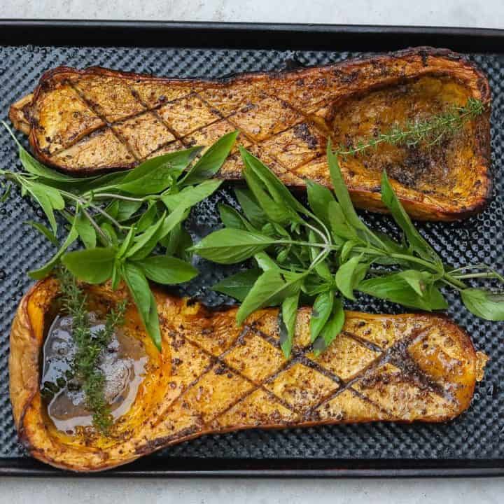 Smoked butternut squash halves on a tray with fresh herbs