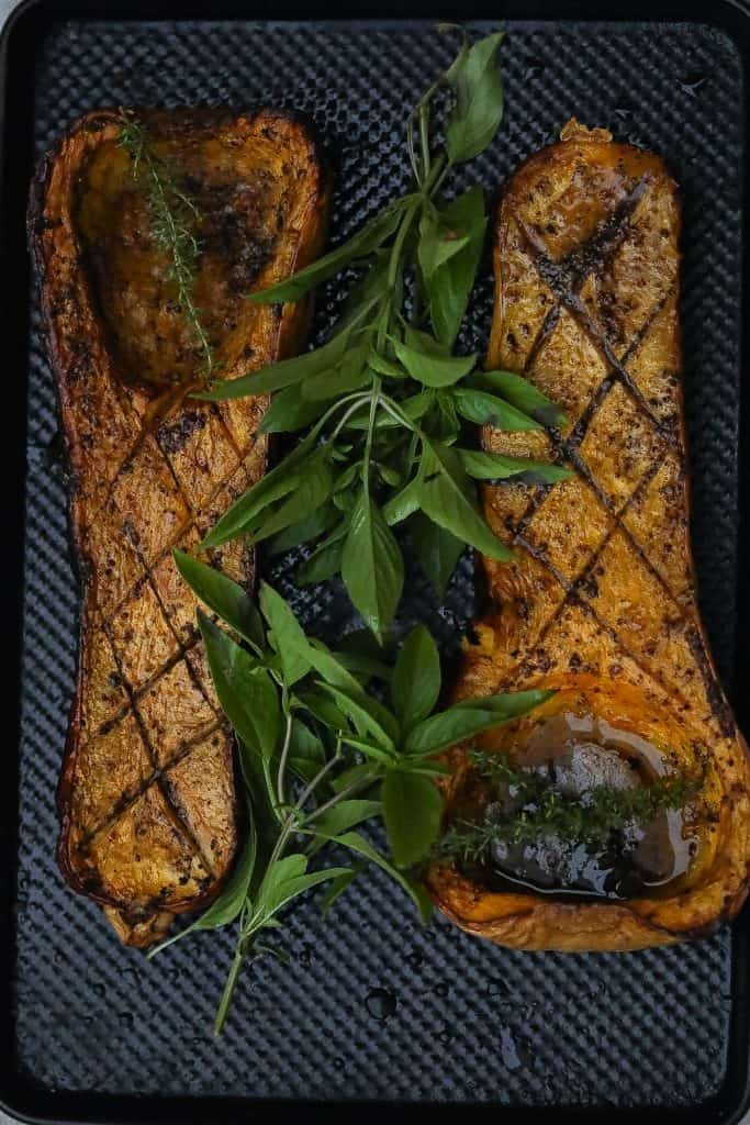 Smoked butternut squash halves on a tray with fresh herbs