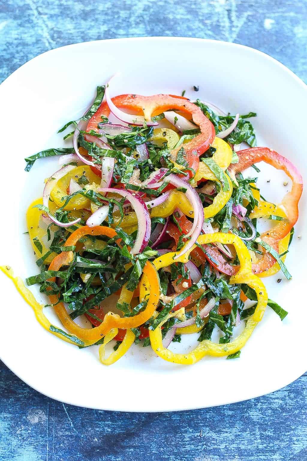 bell pepper salad with collard green strips and red onions on a plate.