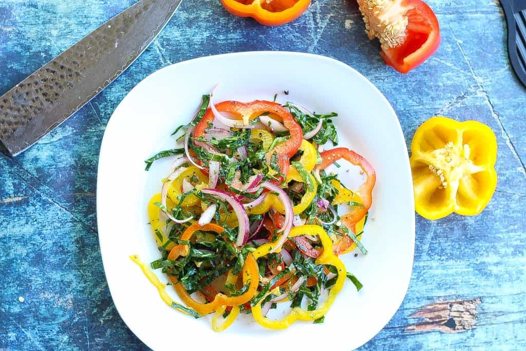 bell pepper salad with collard green strips and red onions on a plate.