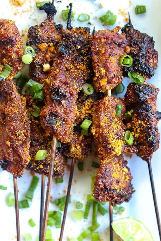 nigerian beef suya kebabs on white plate with green onions
