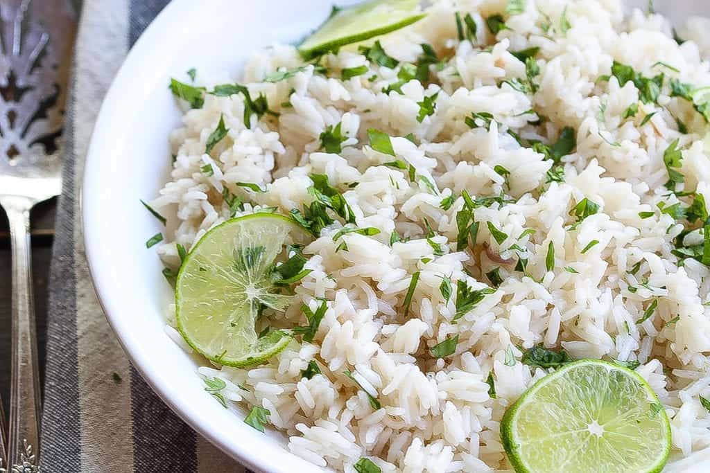 coconut ginger rice in a bowl and topped with limes and cilantro