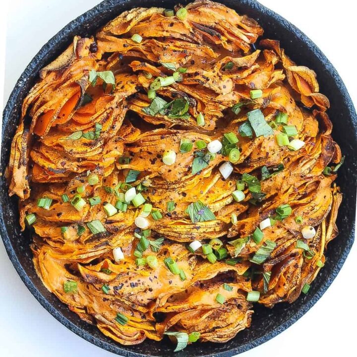 hasselback sweet potatoes in a skillet topped with green onions and red pepper sauce
