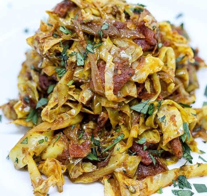indian fried cabbage on a white plate with tomatoes and fresh herbs