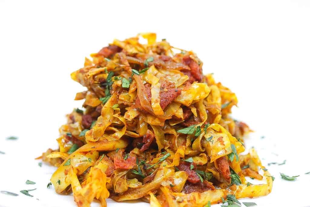 indian fried cabbage on a white plate with tomatoes and fresh herbs