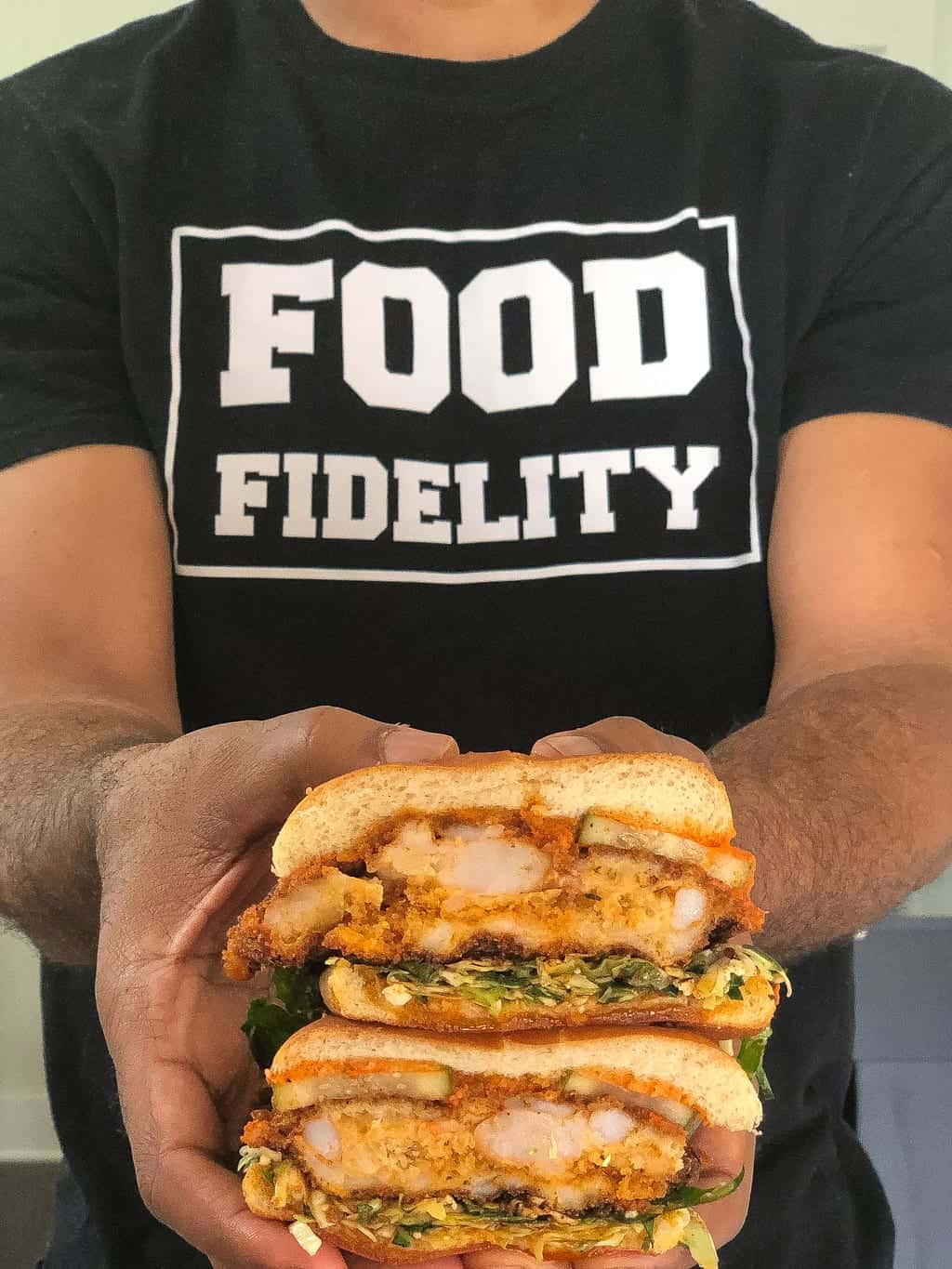 hot shrimp sandwiches being held by guy in a black tshirt