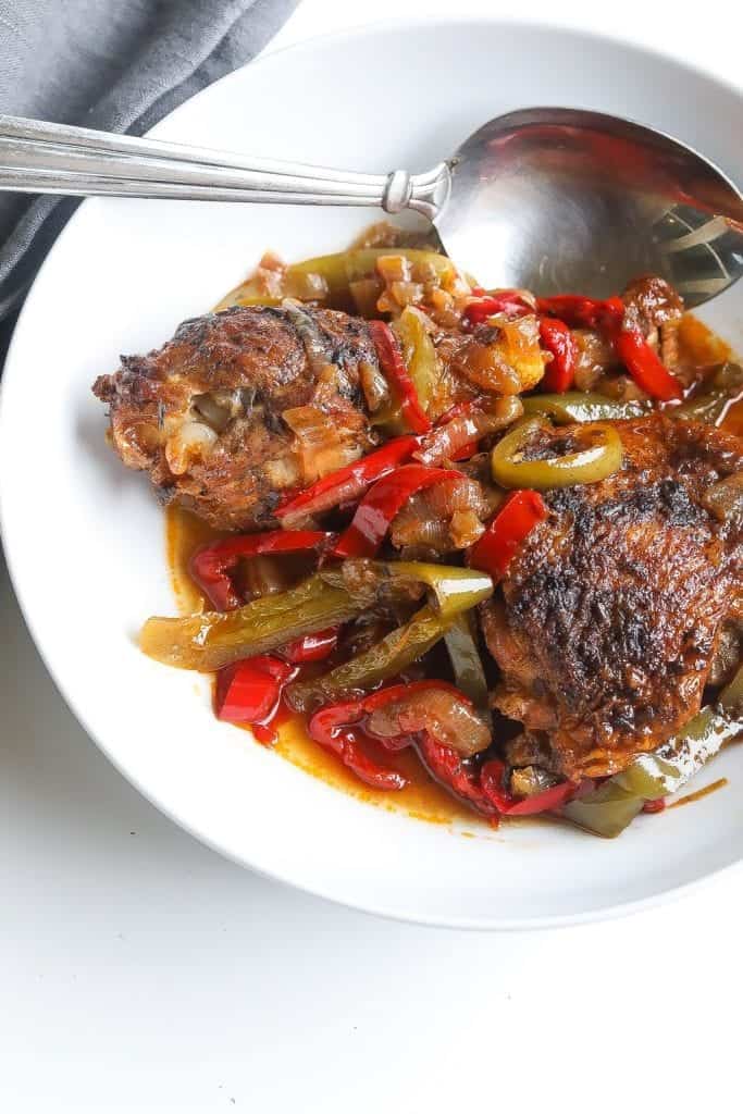 Brown stew chicken topped with peppers in a white bowl