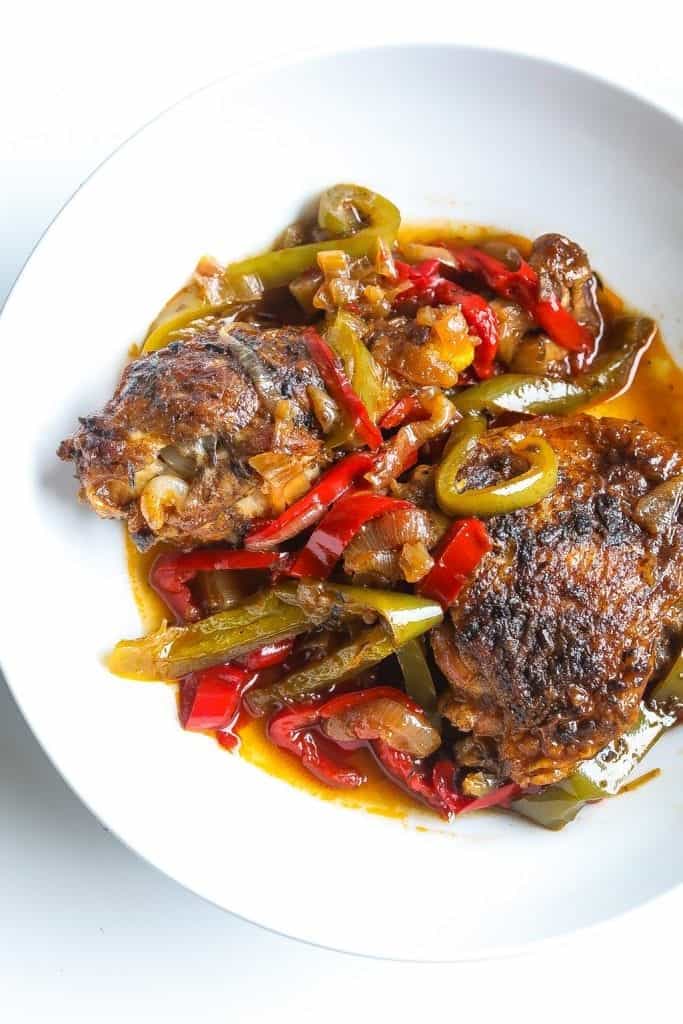 Brown stew chicken topped with peppers in a white bowl