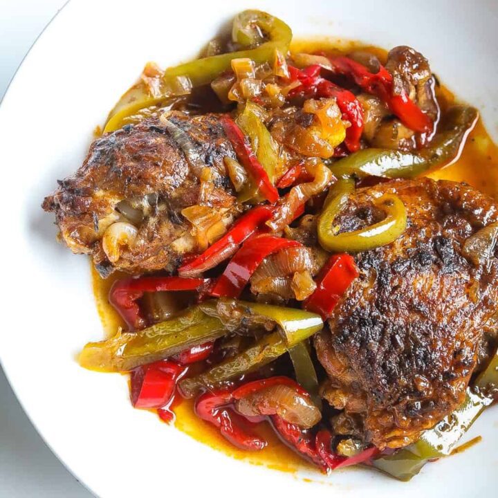 Brown stew chicken topped with peppers in a white bowl