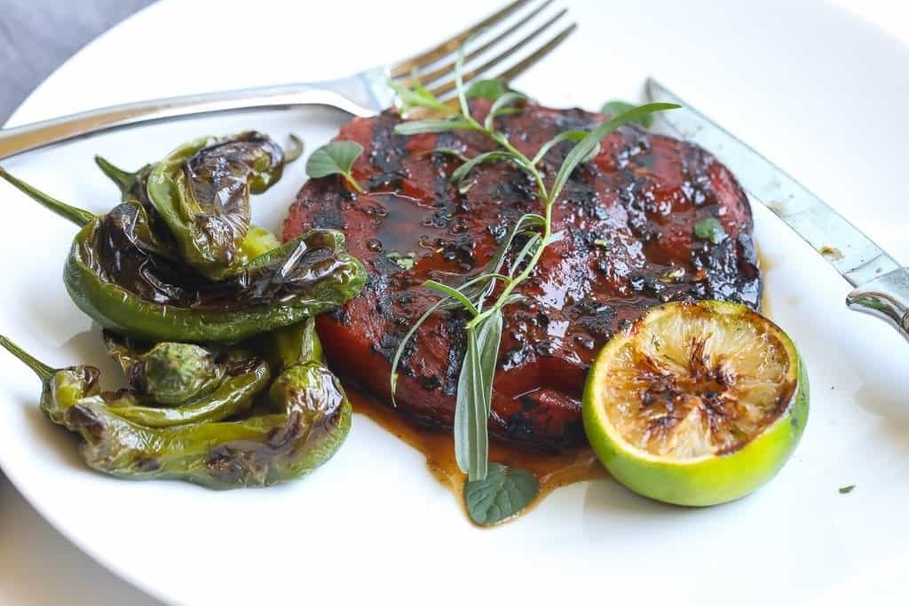 grilled watermelon on a plate with padron peppers and herbs