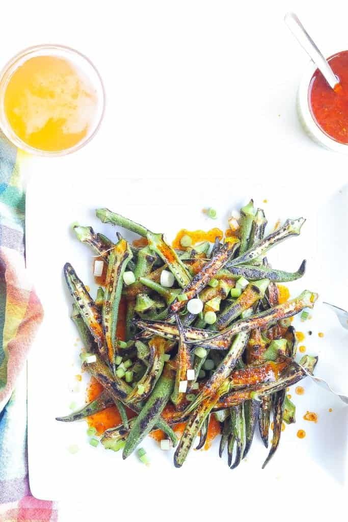 charred okra recipe topped with harissa sauce and green onions on a white plate.