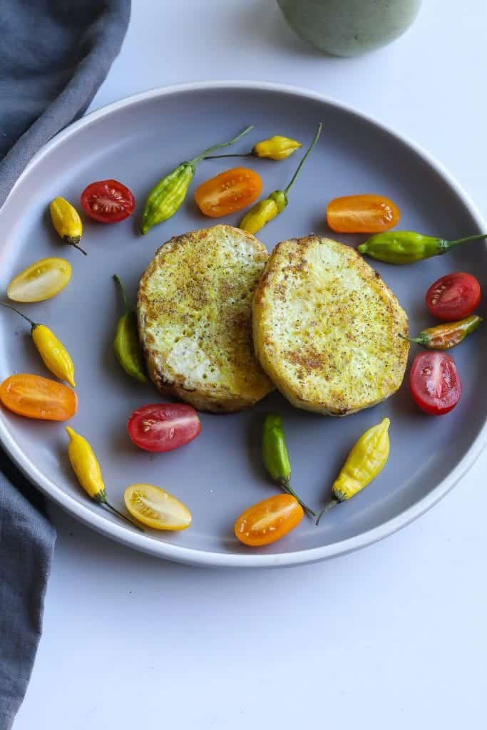 roasted celery steak on a gray plate with tomatoes and peppers