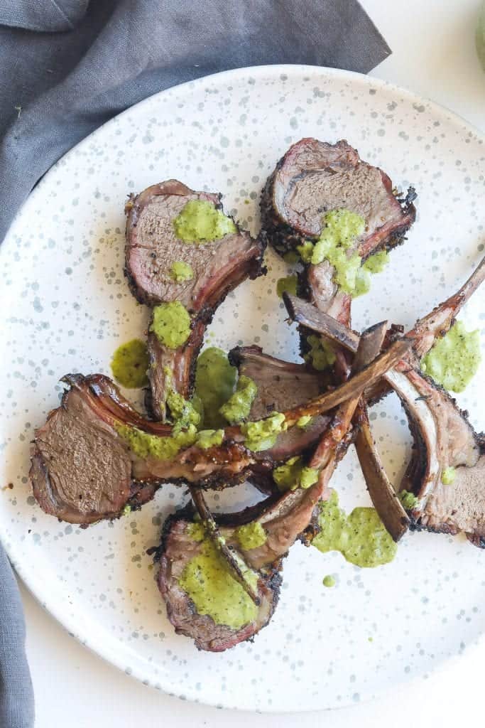 lamb chops on white plate topped with green sauce
