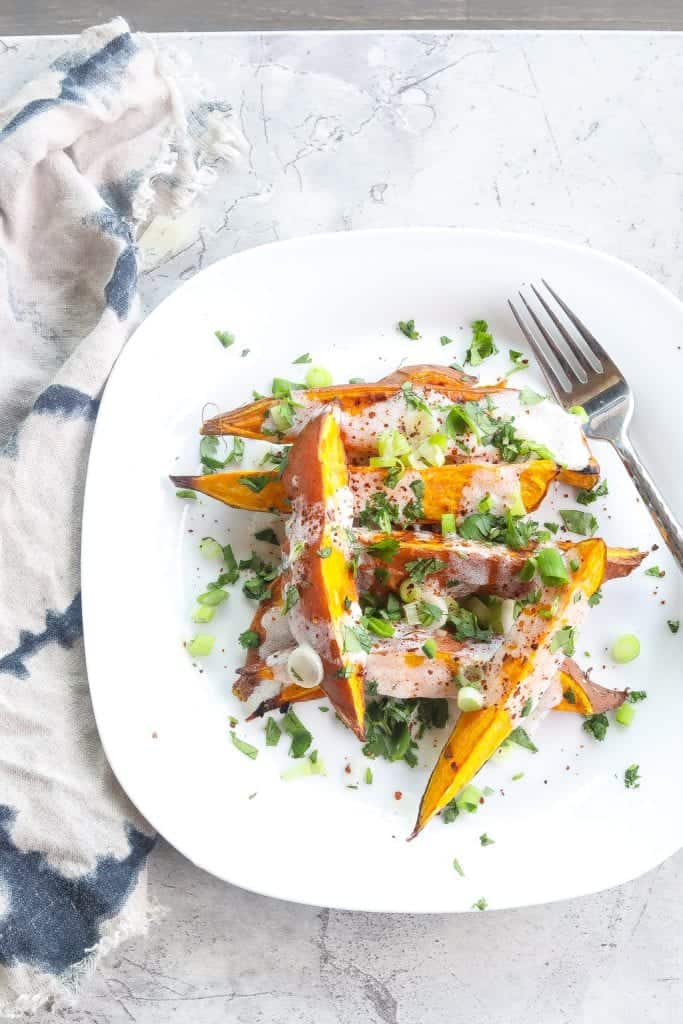 roasted sweet potatoes (wedges) topped with yogurt sauce and green onions on a white plate