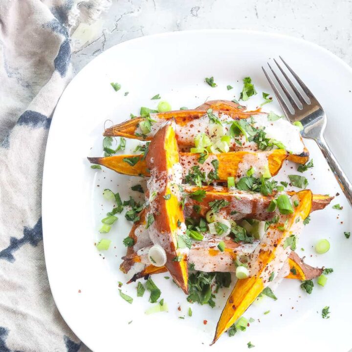 roasted sweet potatoes (wedges) topped with yogurt sauce and green onions on a white plate