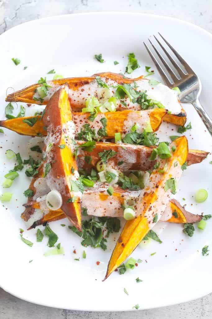 roasted sweet potatoes (wedges) topped with yogurt sauce and green onions on a white plate