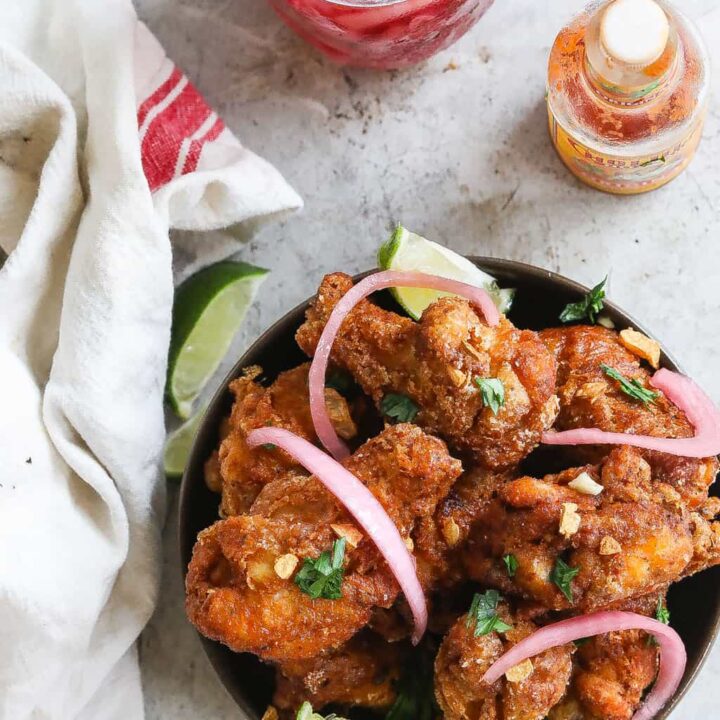 brazilian fried chicken wings (frango a passarinho) in a bowl topped with red onions and cilantro