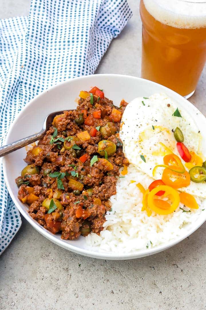 cuban picadillo in a white bowl with rice, fried eggs, and peppers.