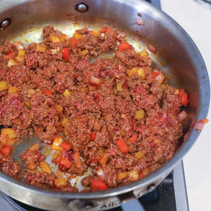 ground beef browning in a skillet with onions and peppers