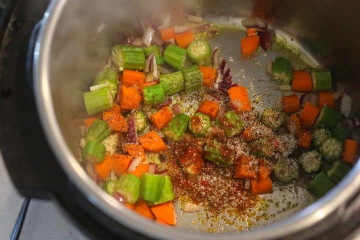 okra, carrots, onions, and garlic sauteing in a pot with spices