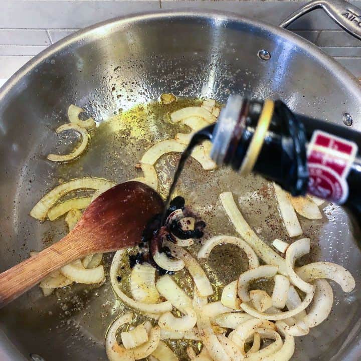 onions cooking in pan while adding balsamic vinegar